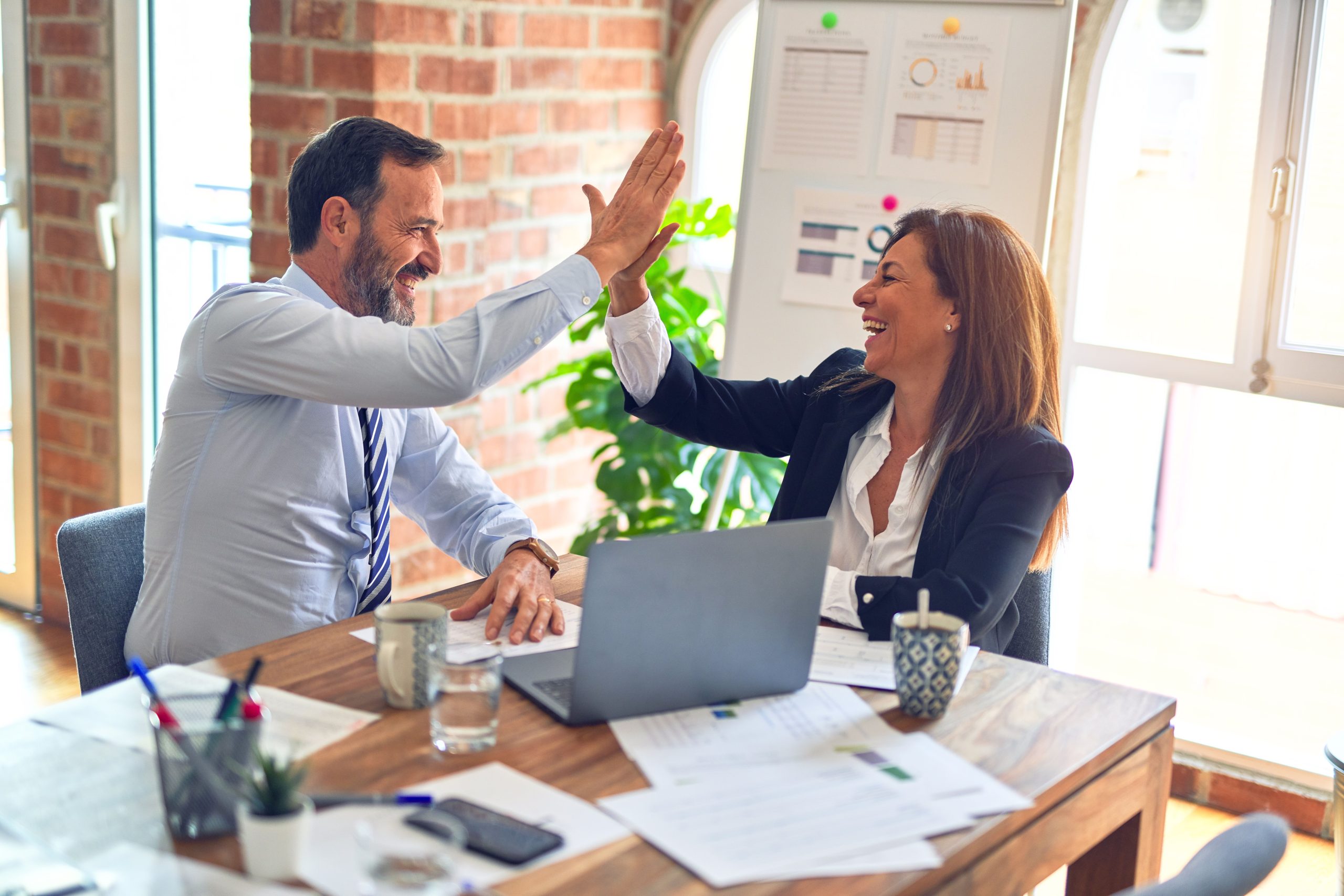 Two business professionals high-five in a modern office celebrating teamwork success.